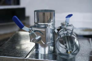 Two manual HVAC dampers with blue handles used to regulate airflow in ductwork.