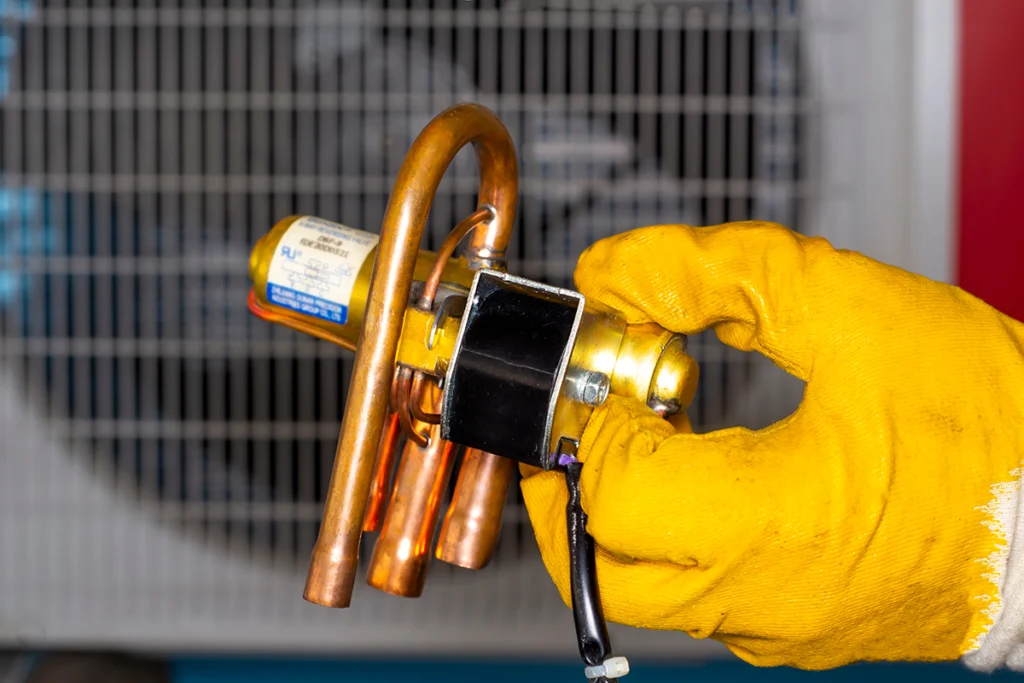 Technician holding a heat pump reversing valve from a heat pump
